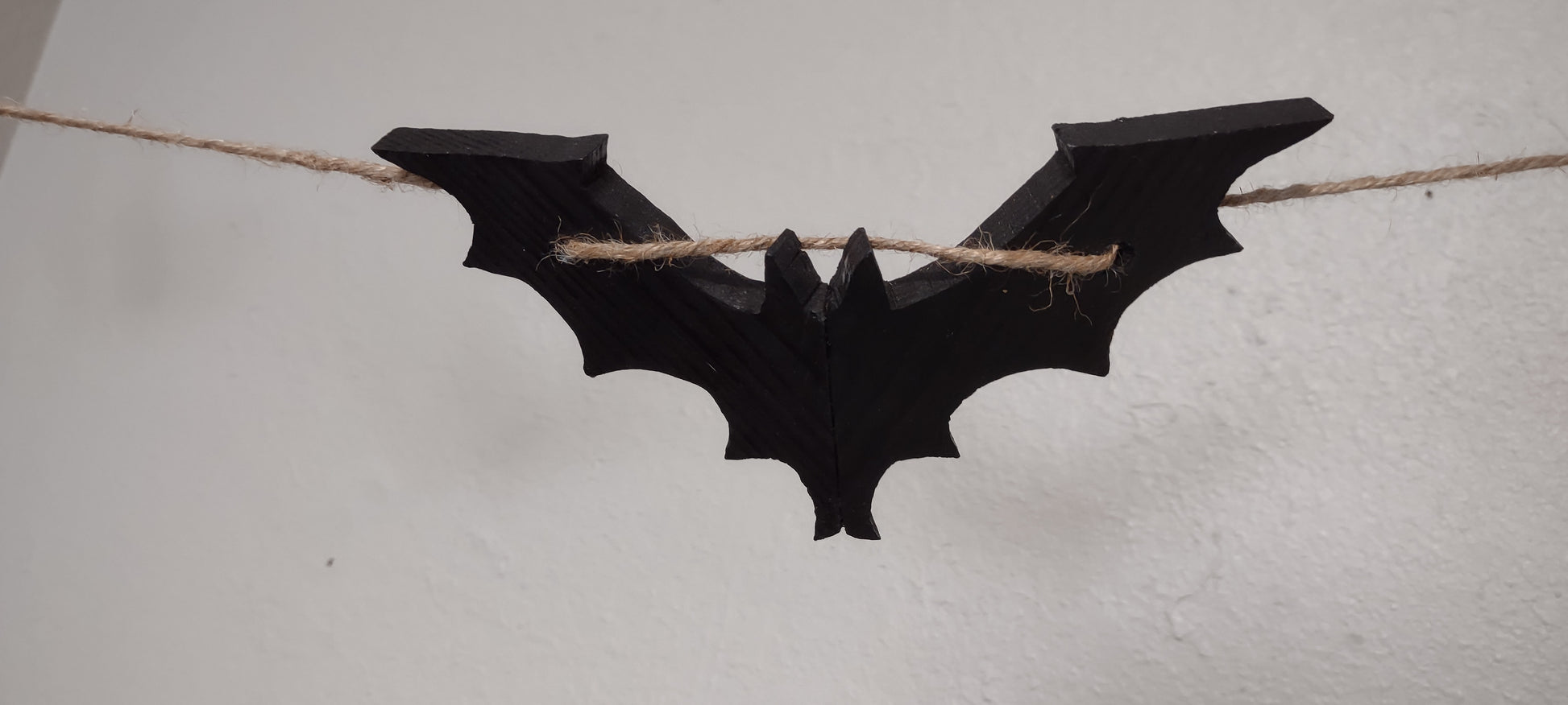 Black, wooden Halloween bat. The wings are angles back for realism.